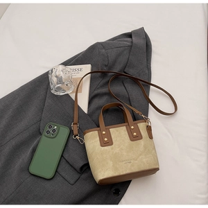 Detail of beige tote bag with leather trim on blazer, showing golden studs and strap