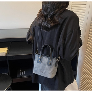 Gray matte bucket bag with black leather handles and studs worn by a model