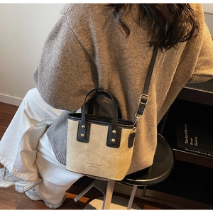 Chic beige and black bucket bag with gold rivets worn with a cozy autumn sweater