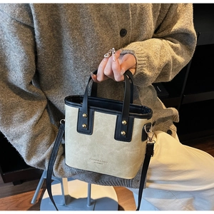 Close-up of beige and black bucket bag with gold rivets and leather handle