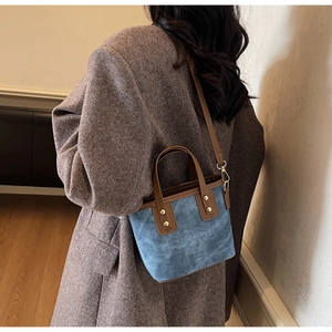 Detail of blue textured tote bag with brown leather trim and golden rivets shown on model