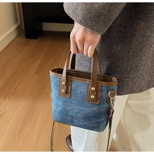 Detail of denim mini tote bag with brown leather handles and golden metal rivets