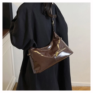 Détail d'un sac hobo marron foncé brillant avec fermeture éclair dorée porté