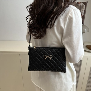 Chic black quilted crossbody bag with a gold bow accent and slender shoulder strap