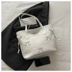 Detail view of white quilted tote bag with colorful bows and drawstring on a suit jacket