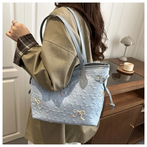 Light blue tote bag with embossed E-letters and colorful woven bow details in a home setting
