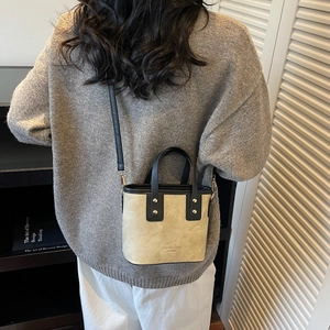 Minimalist beige crossbody bucket bag with black straps worn by a model in casual style