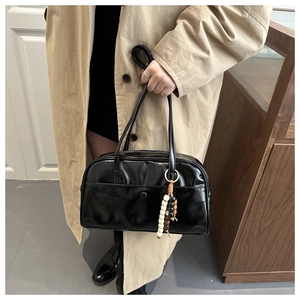 Detail of a black glossy shoulder bag with a unique wooden bead tassel and snap button