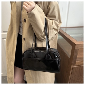 Detail of minimalist black patent leather shoulder bag styled with a beige trench coat