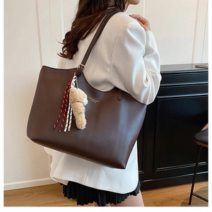 Detail of deep brown leather tote bag with gold logo and plush animal charm
