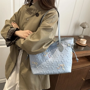 Light blue quilted tote bag with bow embroidery shown on a model in a minimalist interior