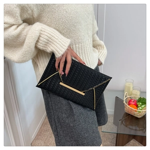 Détail de la pochette enveloppe noire tressée avec garniture métallique dorée élégante