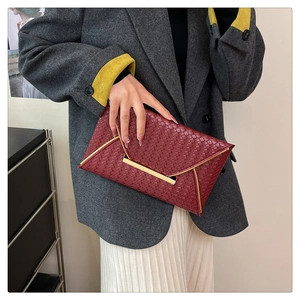 Détail d'une pochette enveloppe tressée bordeaux avec boucle dorée et texture chic