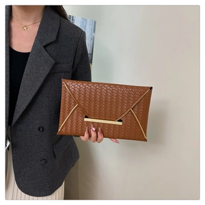 Détail d'une pochette tressée marron avec bordure dorée tenue par un mannequin élégant