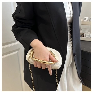 Detailed view of cream evening clutch with a bold gold circular handle and metal chain strap