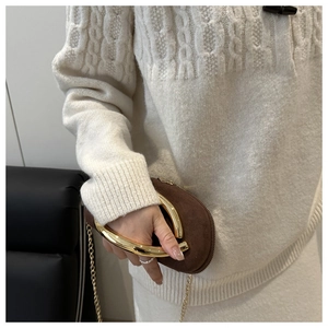Detail of brown suede handbag with large gold circular handle and fine metal chain