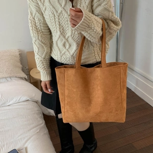 Brown suede tote bag side view being carried by a model in a cozy indoor setting