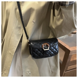 Detail einer schwarzen gesteppten Mini-Umhängetasche mit Goldschnalle an einem Trenchcoat
