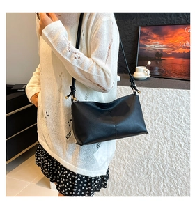 Detail of black pebbled leather crossbody bag with knot strap and gold metal hardware