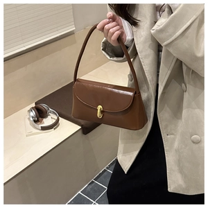 Detail of a brown glossy leather shoulder bag featuring a gold metal twist lock buckle