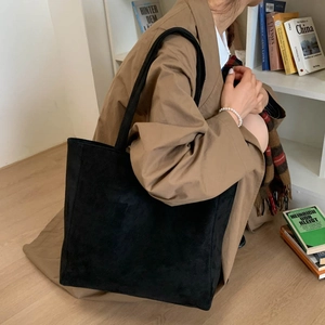 Large black suede tote bag with slim shoulder strap shown in a cozy interior setting