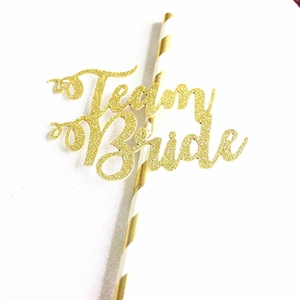 Détail macro du cake topper Team Bride doré pailleté avec sa paille de support rayée