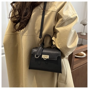 Detail view of a black lychee texture crossbody bag with gold ring lock on a beige coat