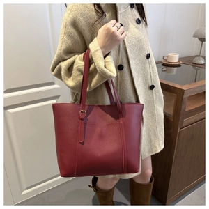 Model wearing a burgundy matte leather tote bag with long straps in a cozy room