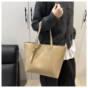 Detail of minimalist cream tote bag showing adjustable strap and front pocket design