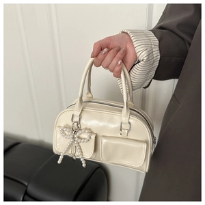 Detail of cream white handbag featuring a pearl bow pendant and glossy finish texture