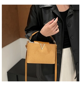 Detail der senfgelben Beuteltasche mit metallischem V-Logo und rundem Handgriff