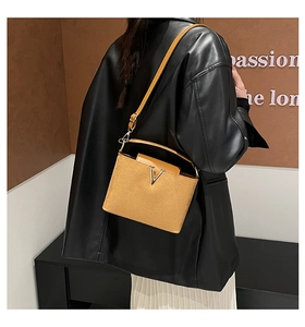 Detailansicht der braunen Wildledertasche mit goldener V-Schließe und Lederjacke