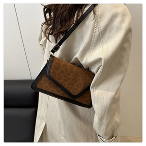 Detail of leopard print shoulder bag with black leather trim worn on a beige coat