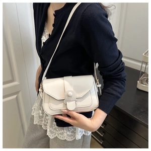 Detail shot of a white crossbody bag featuring an oval decorative clasp and stitched flap