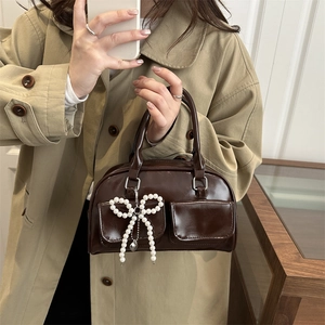 Dark brown leather boston handbag with pearl bow pendant worn with a trench coat