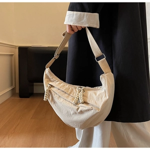Détail du sac demi-lune beige en nylon montrant les plis et la tirette en corde tressée