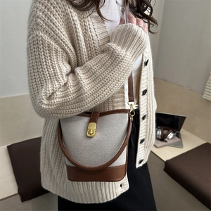 Minimalist canvas bucket bag with brown leather trim and golden clasp, styled on model