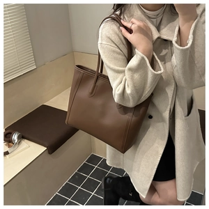 Brown leather tote bag with vertical stitching shown in a warm minimalist indoor setting