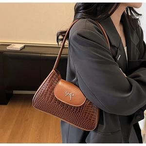 Brown crocodile pattern shoulder bag featuring silver bow detail on gray blazer model