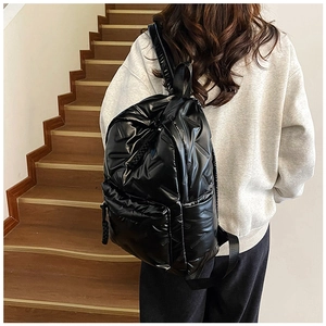 Side view of a glossy black puffer backpack with quilted texture on female model