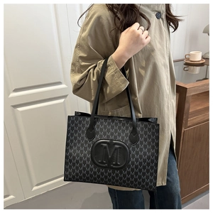 Detail of black tote bag featuring repetitive M letter print and round M logo embossed