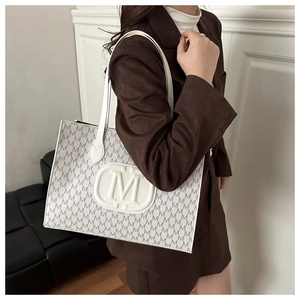 Detail of white tote bag with letter M monogram print shown on model in brown blazer
