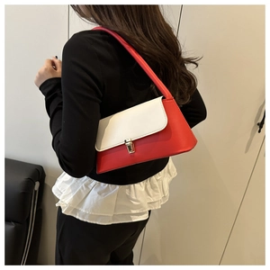 Detail of a red and white leather baguette bag with a gold buckle worn on the shoulder