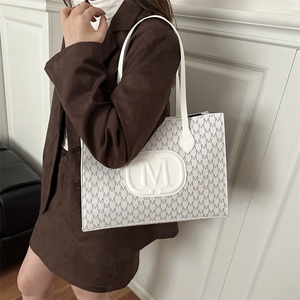White tote bag with grey M-letter print and oval logo shown on shoulder with dark suit