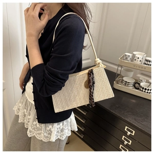 Close-up of beige woven shoulder bag with side tassel detail and metal hardware accents