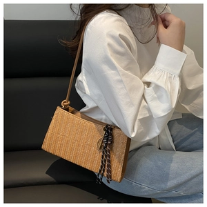 Detailed view of woven straw shoulder bag with leather strap and tassel ornament