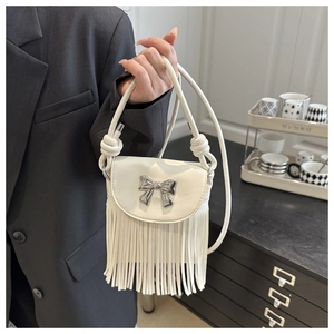 Close-up of white crossbody bag featuring silver bow accent and long fringe tassels