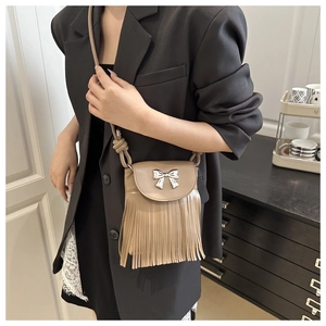 Detail of milk tea leather crossbody bag featuring silver bow buckle and long tassels