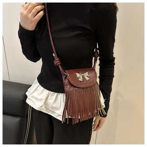 Detail of dark brown crossbody bag with metal bow and long stylish tassels