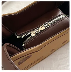 Macro detail of high-quality gold metal zipper and textured leather stitching on brown bag